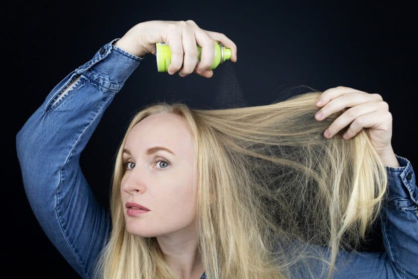 Une jeune femme blonde vaporise du shampoing sec sur ses cheveux